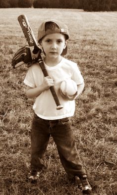 a young boy holding a baseball bat and ball in his hands while standing on the grass