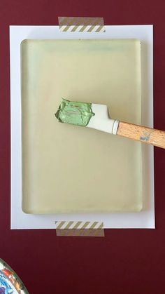 a painting brush sitting on top of a piece of white paper with green paint in it