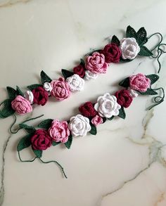 two crocheted flowers are laying on a marble counter top, one is pink and the other is white