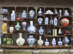 many vases are on display in front of a brick wall and wooden shelves with different designs