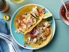 two fish tacos on a blue plate next to a bowl of salsa and lime wedges