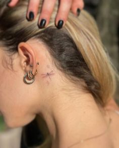 a woman's ear has a small cross tattoo on it