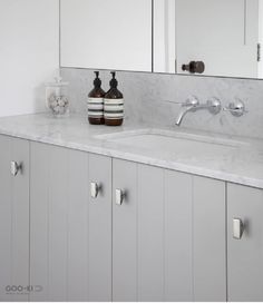 a bathroom with white cabinets and marble counter tops, two soap dispensers on the sink