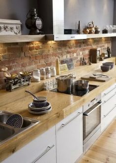 a kitchen with white cabinets and wooden counter tops, along with a brick wall in the background