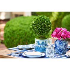 a blue and white table setting with pink flowers in a vase, plates and utensils