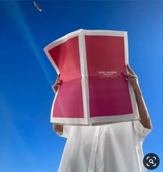 a person holding up a large piece of paper in front of their face with the sky behind them