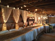 a long table covered in white linens under lights and draping on the ceiling