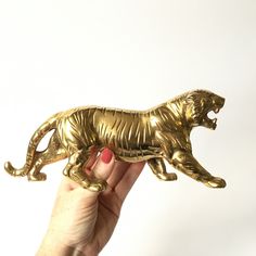 a hand holding a gold figurine of a tiger on its hind legs, against a white background