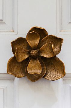 a metal flower mounted to the side of a white door with gold paint on it