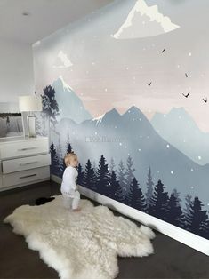 a baby standing in front of a wall mural with mountains and birds painted on it