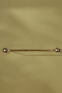 a gold tie bar on a tan surface with two white beads hanging from it's end