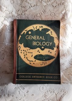 an old book with the title general biology written in gold on it sitting on a lace covered surface