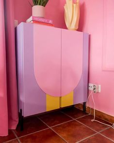 a pink and yellow cabinet with flowers on top next to a phone plugged in