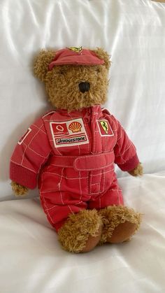 a teddy bear wearing a red suit and hat sitting on a white bed with sheets