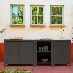 a sideboard with two windows and plates on it in front of a house that has red tile flooring