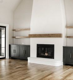 an empty living room with white walls and wood floors, fireplace in center area between two black cabinets