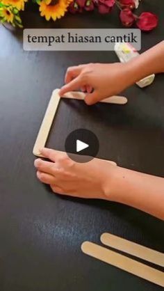 a woman is cutting out popsicle shapes on a black table with flowers in the background