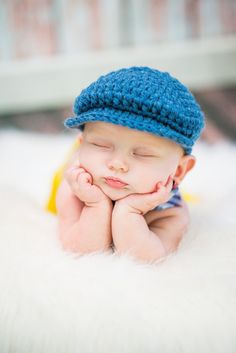 a baby wearing a blue crochet hat is laying on his hands and looking at the camera