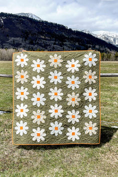 a quilted blanket sitting on top of a grass covered field