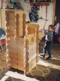 a young boy standing in front of a wooden structure that is made out of plywood