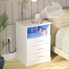 a white night stand with blue drawers and a plant on it next to a bed