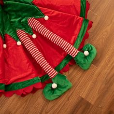 a red and green christmas tree skirt laying on the floor next to a wooden floor