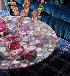 a glass table with vases and flowers on it in front of a blue couch