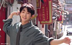 a young man is standing in the street with his hands on his head and smiling at the camera