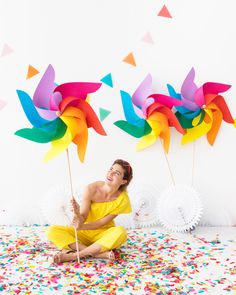 a woman sitting on the floor with two pinwheels in front of her and confetti all around her