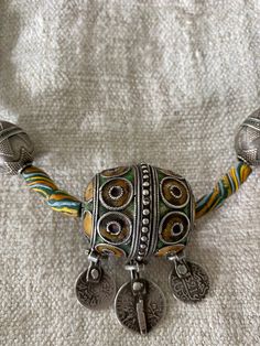 This beautiful necklace has a central Moroccan enamelled egg bead from which dangle some early 20thC silver coins, French and Arabic. I have put it together with some vintage African trade beads which pick out the colours of the enamel. I have also included some fine silver egg shaped Afghan Turkmen beads which again compliment the egg shaped central bead. Although made up from elements from different traditions and continents the whole is remarkably harmonious and charming. Vintage Handmade Silver Beads, Handmade Vintage Silver Beads, Silver Amulet Style Beaded Necklace, Silver Beaded Amulet Necklace, Unique Silver Necklace With Colorful Beads, Unique Silver Necklaces With Colorful Beads, Vintage Silver Beaded Necklaces With Colorful Beads, Unique Silver Necklace With Dangling Beads, Silver Large Beads Amulet Style