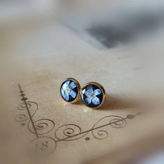 a pair of blue flower stud earrings sitting on top of a piece of paper