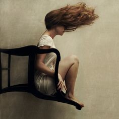 a woman is sitting on a chair with her hair blowing in the wind