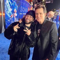 two men standing next to each other in front of a blue carpeted area with an advertisement for sonic the movie