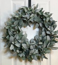 a wreath hanging on the front door of a house with white doors and green leaves