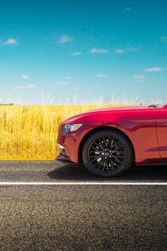 a red sports car is parked on the side of the road in front of a wheat field