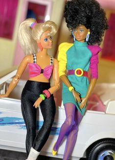 two barbie dolls standing next to each other in front of a white car with the door open