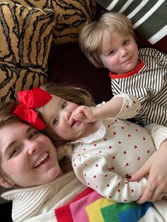 a woman and two children laying on top of a couch with one holding the other