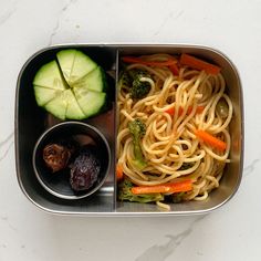 a metal container filled with pasta and veggies on top of a white table