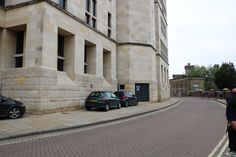 two cars parked on the side of a road next to a tall building with columns