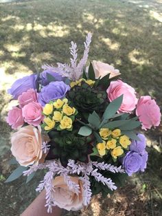 a bouquet of flowers in someone's hand on the grass with trees in the background