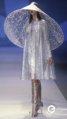 a woman in a white dress and hat walking down a runway