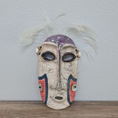 a mask with feathers on it sitting on a wooden table in front of a white wall