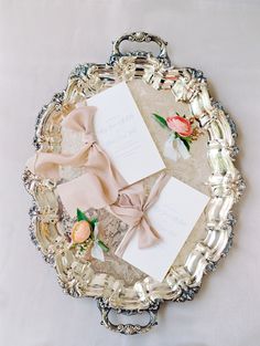 the wedding stationery is displayed in an ornate silver tray with ribbon and flowers on it