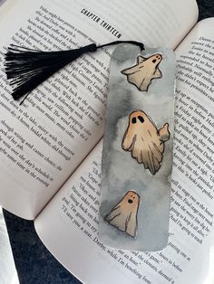 a bookmark with ghost faces and tassels on top of an open book