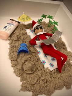 the elf is laying in the sand with his feet up and some toys around him