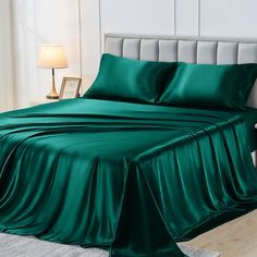 a bed with green sheets and pillows on top of it in a room next to a lamp