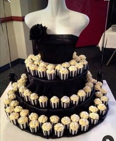 a three tiered cake with white cupcakes on it and black ribbon around the bottom