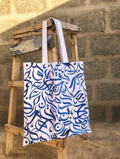 a blue and white tote bag hanging from a wooden easel in front of a brick wall