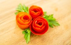 three orange flowers sitting on top of a wooden table next to green leafy stems