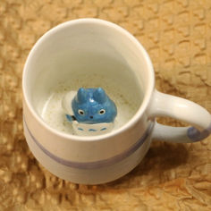 a small blue elephant sitting inside of a white cup on top of a brown table